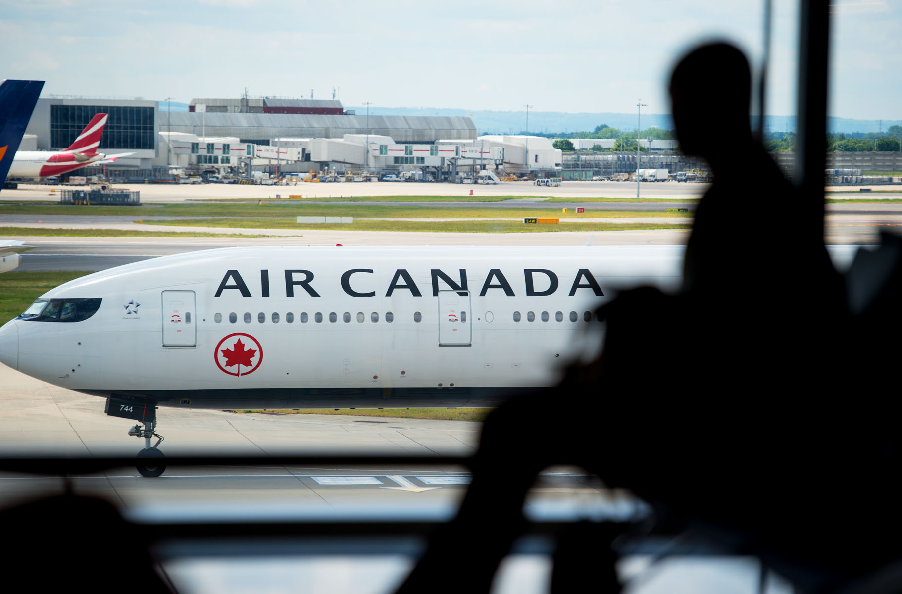 Heathrow, T2A, airside, passenger silhouetted, Air Canada aircraft taxiing in background, May 2019. Photo Credit: Air Canada.