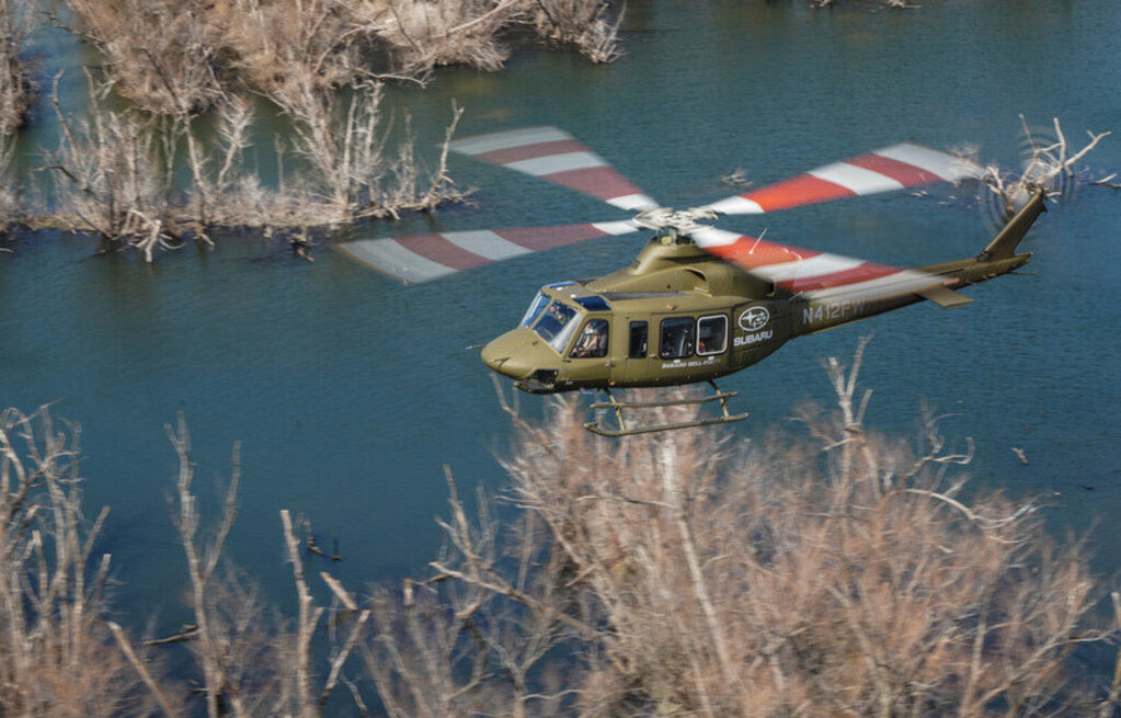 A SUBARU Bell 412EPX helicopter flies over a lake.