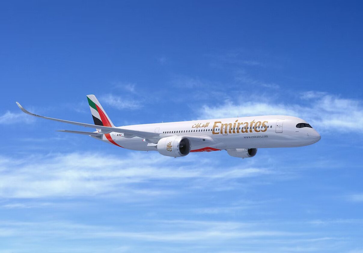 An Emirates A350 in flight against a blue sky.