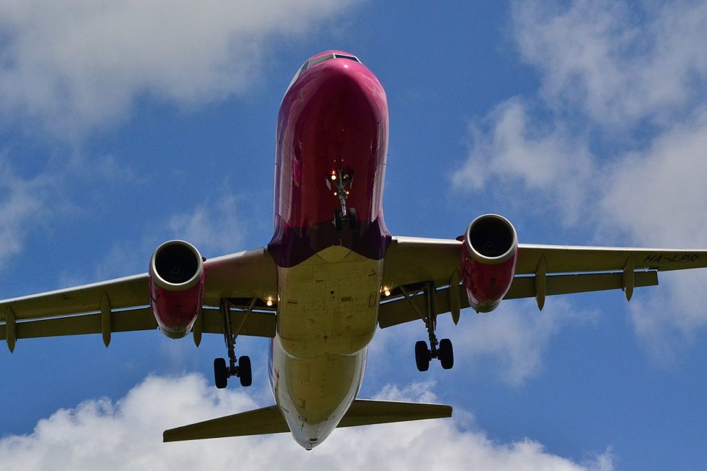 A Wizz Air aircraft passes overhead in a blue sky.