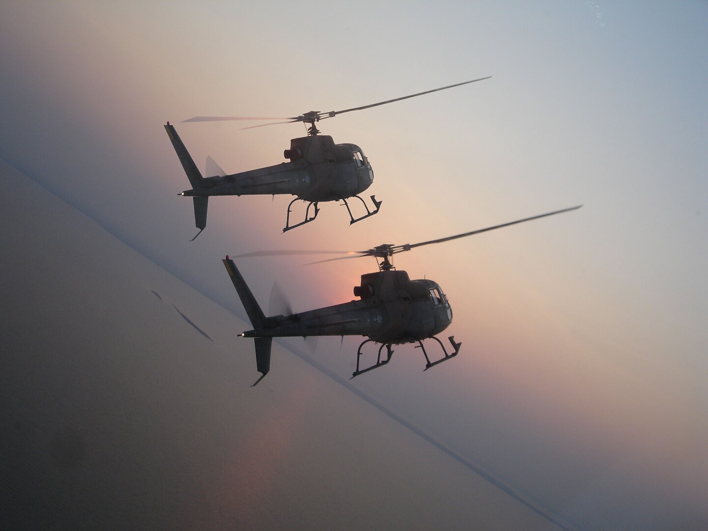 Two Brizilian Armed Forces H125 helicopters bank in formation.