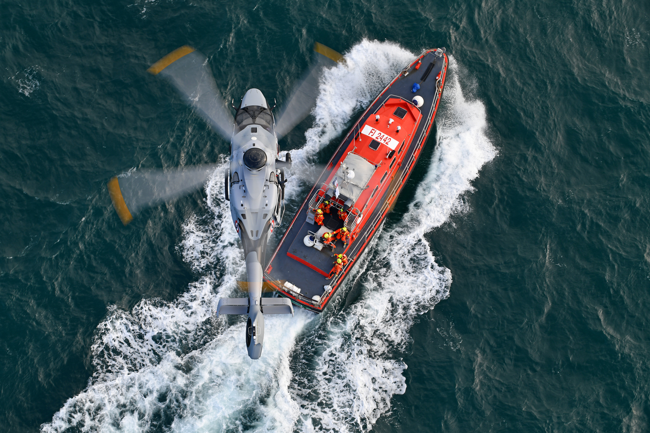 And Airbus H160 helicopter hovers over a search and rescue boat.