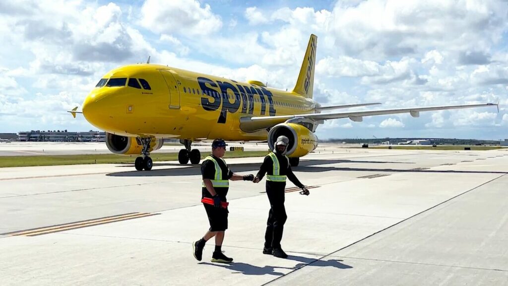 Ground staff and a Spirit Airlines aircraft parked on the ramp.