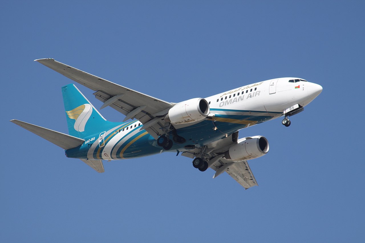 An Oman Air 737 passes overhead.