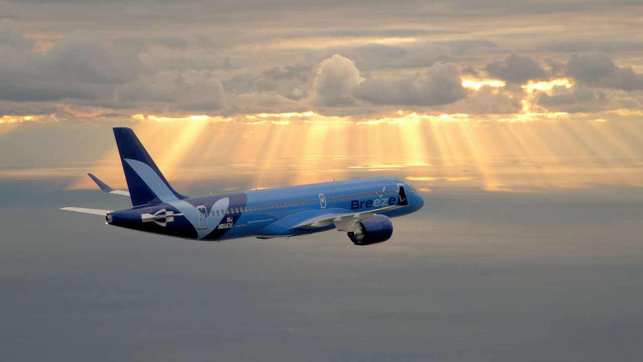 A Breeze Airways A220 flies into the sunset.