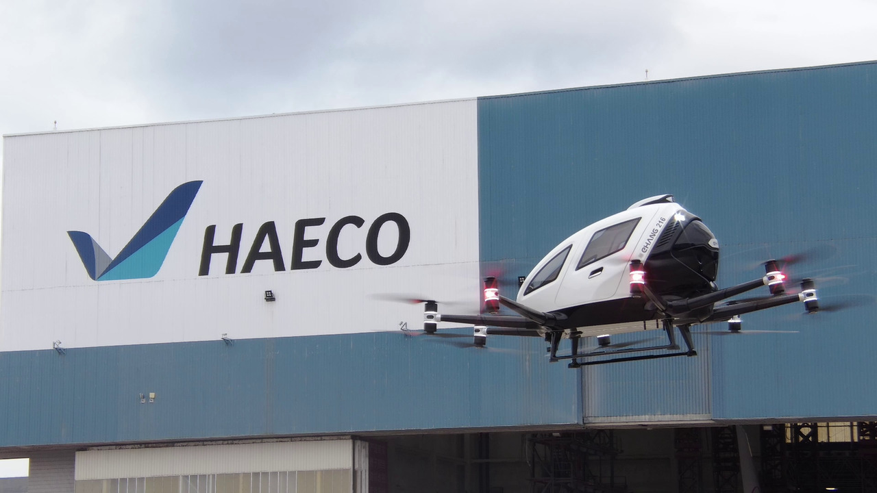 The EHang prototype AAV eVTOL aircraft hovers in front of a HAECO building