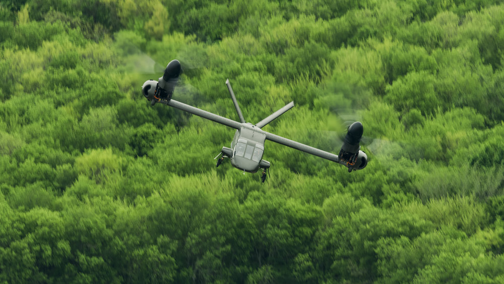 A US Army Bell V-280 Valor tiltrotor in flight over forest.
