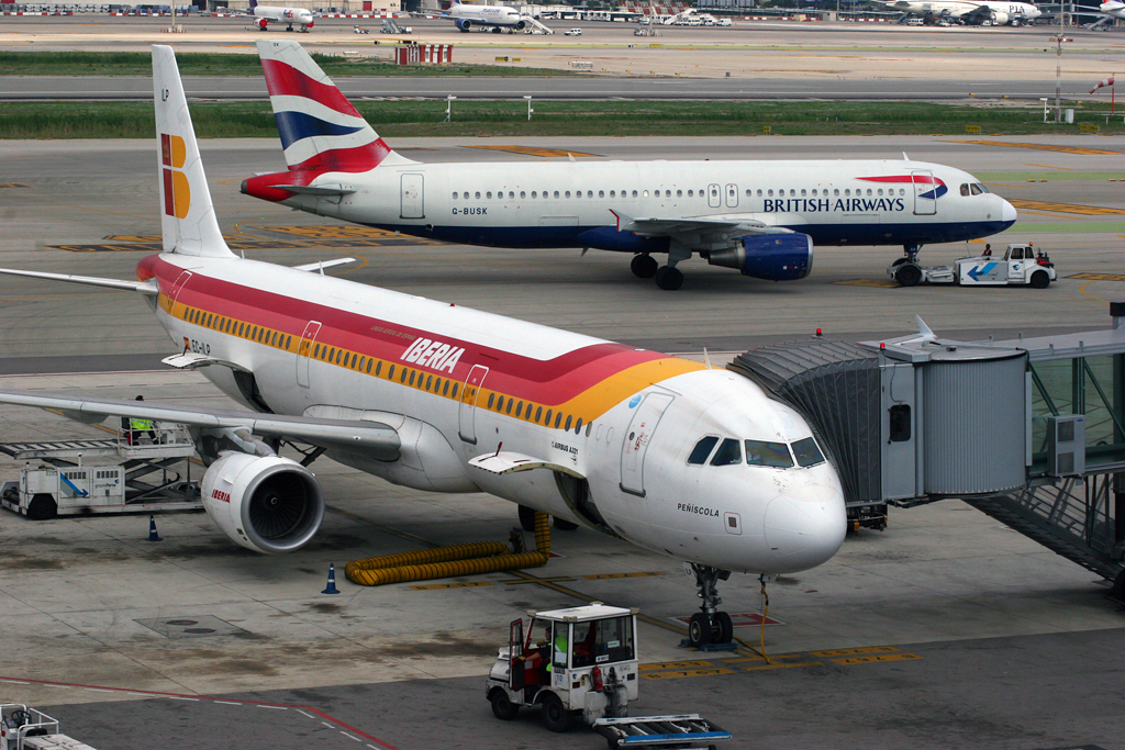 A British Airways A320 taxis past an Iberia A321 parked at the terminal.