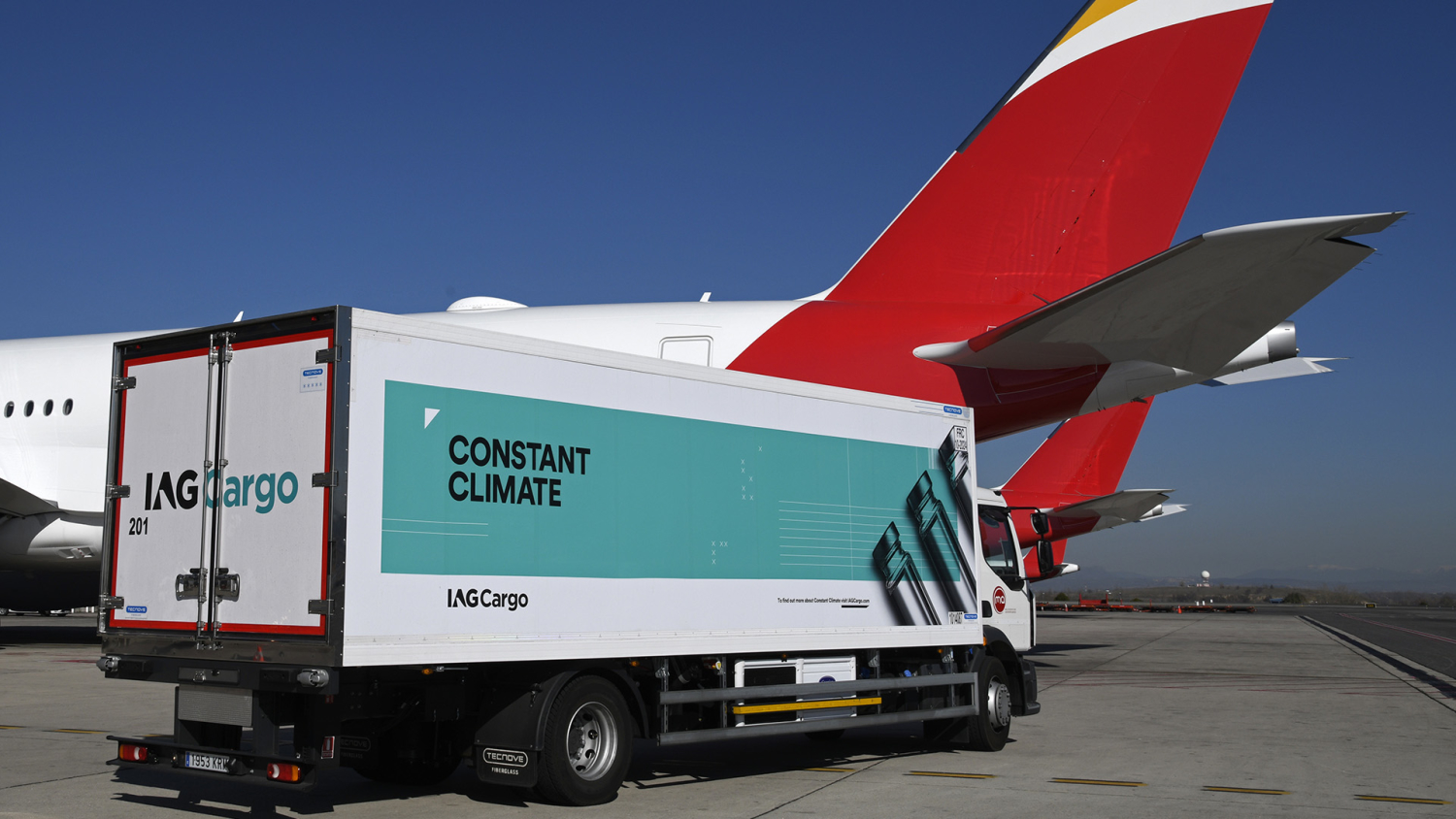 An IAG Cargo vehicle parked next to an Iberia passenger aircraft.