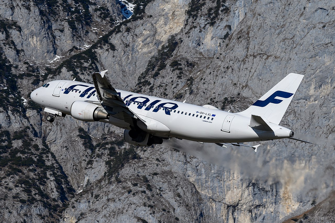 A Finnair Airbus A220 climbs against mountains.
