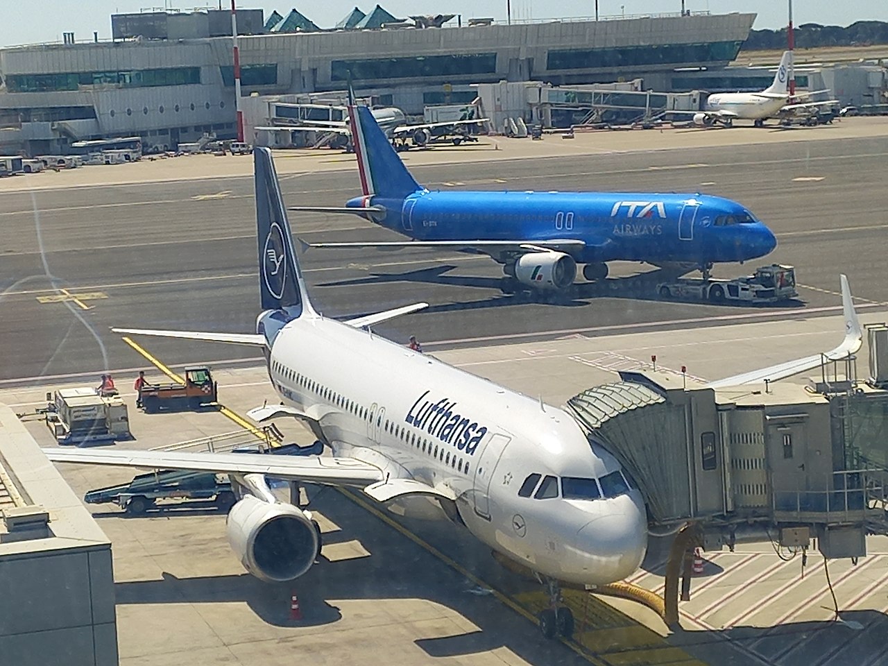 An ITA Airways aircraft taxies past a Lufthansa aircraft parked at the terminal.