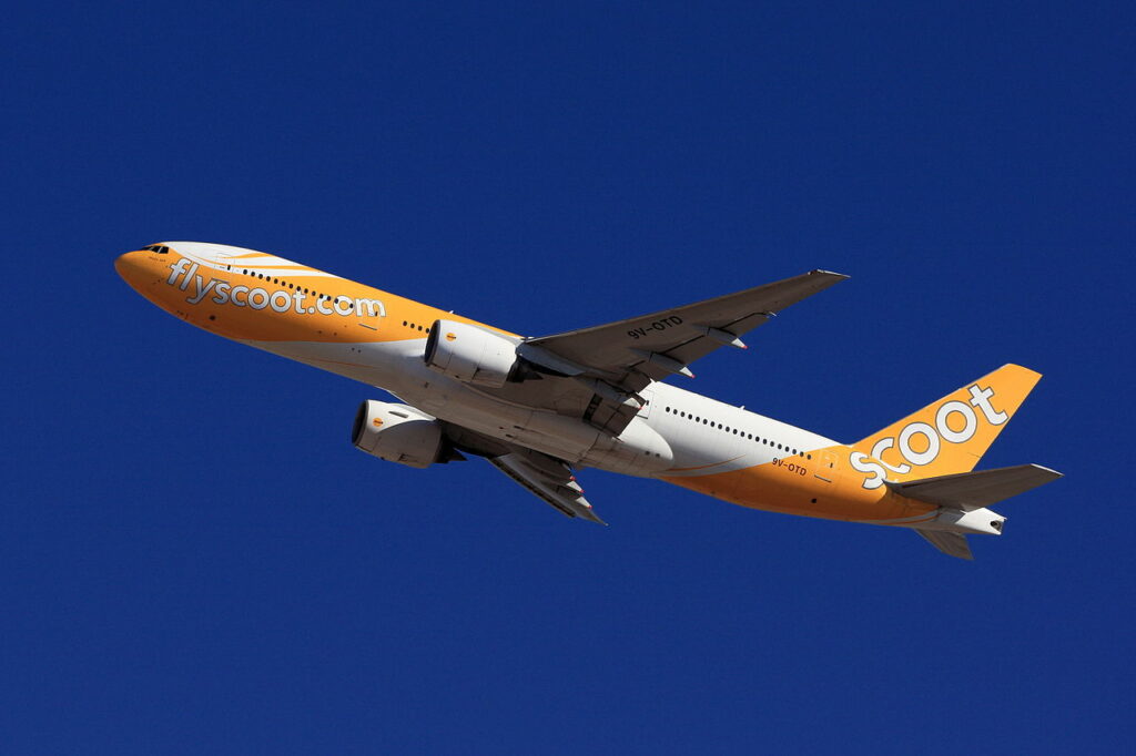 A Scoot Airlines Boeing 777 climbs in a blue sky.