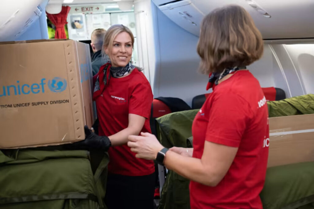 Norwegian flight attendants handle UNICEF boxes on aircraft.