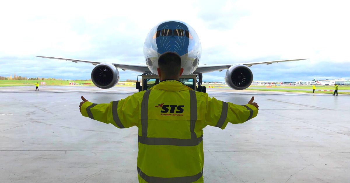 An STS Aviation Services staff member marshals a taxiing aircraft.