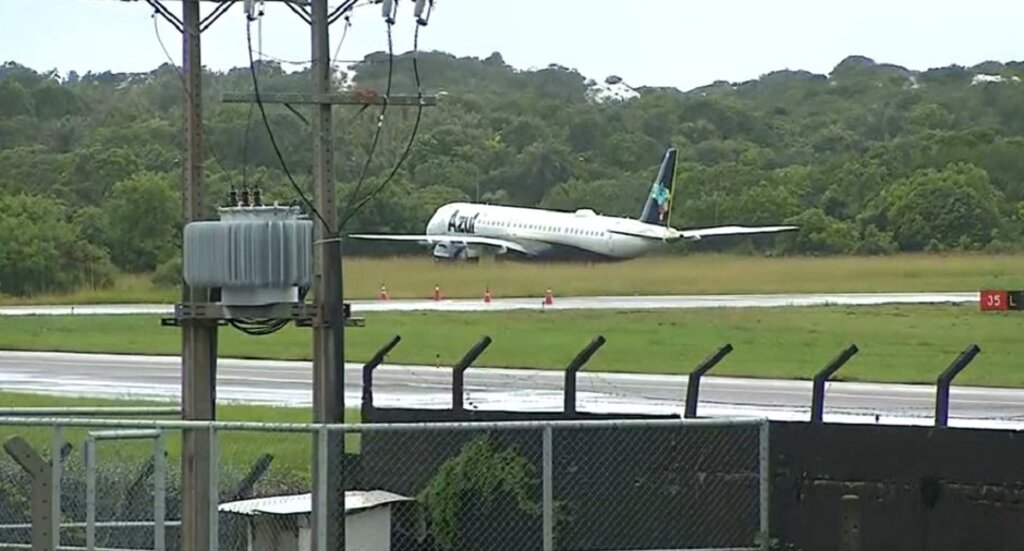 An Azul Airlines Embraer E195 lies in grass at the end of the runway.