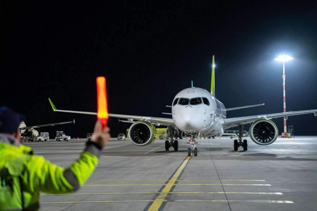 An airBaltic A220 is marshalled to the parking bay.