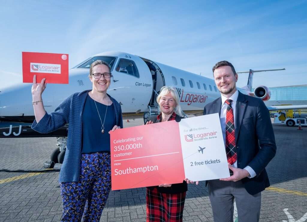 Loganair 350,000th Southampton Airport customer stands with airline staff in front of aircraft.