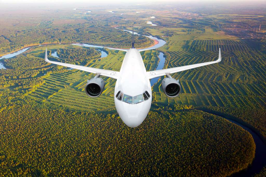 A plane flies against a background of a forest and river.