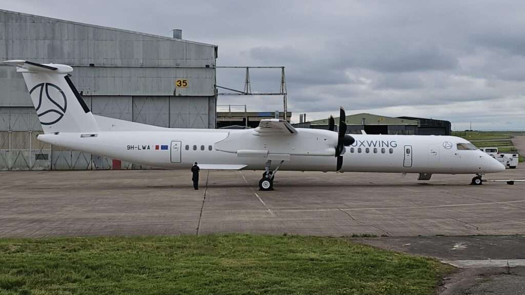 A Luxwing DHC 8-400 parked in front of the hangar.