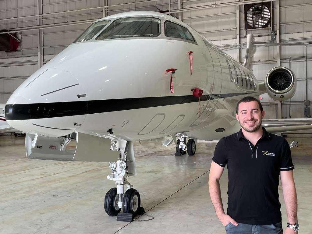Caio Holtz of BitLux stands with a private jet in the hangar.