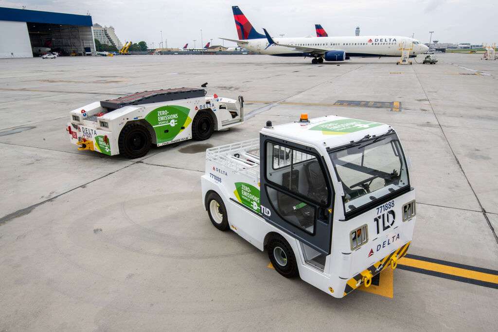 A Delta Air Lines aircraft and two tugs on tarmac.