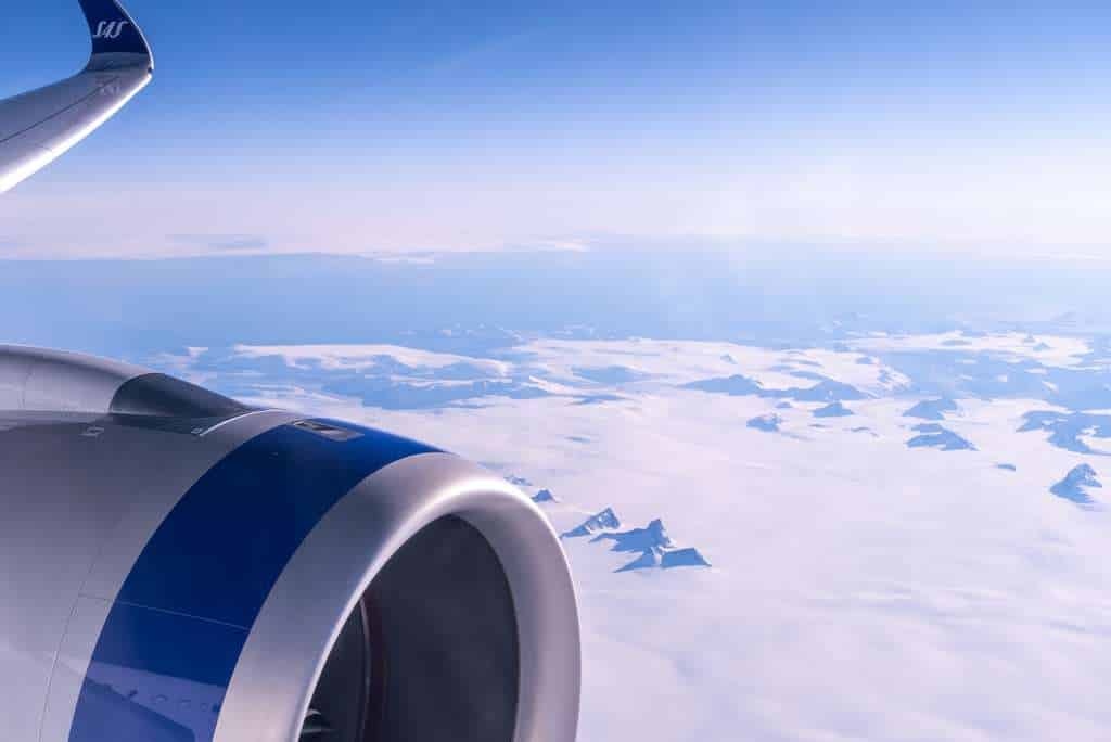 View over SAS aircraft engine in flight over snowy mountain.