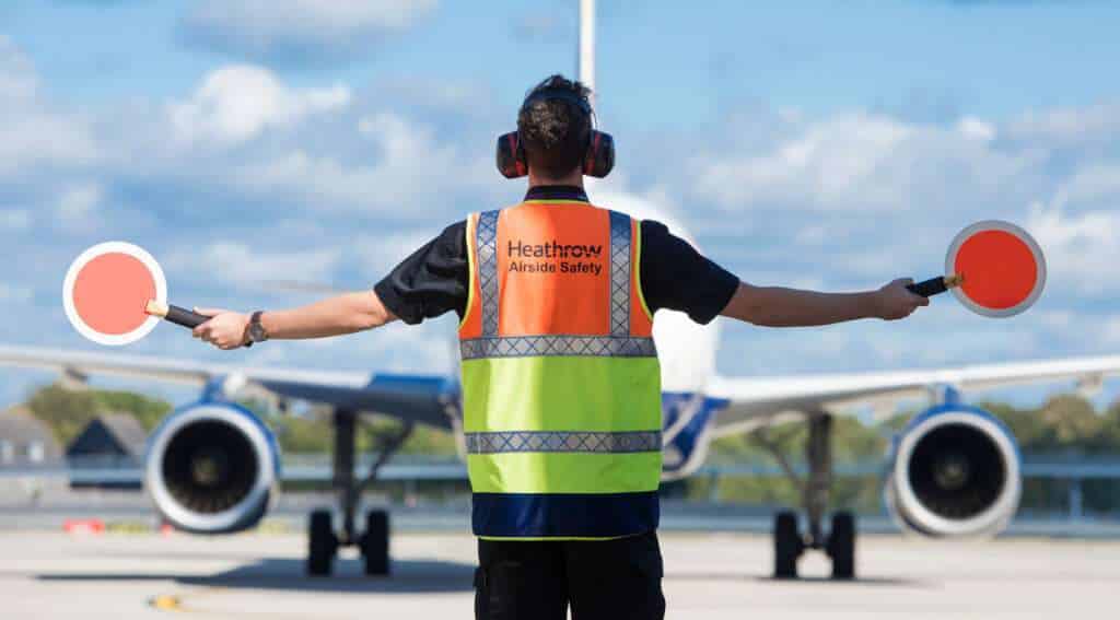 A Heathrow Airport ground handler marshals an aircraft.