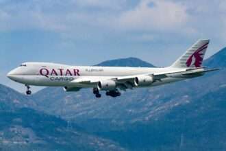 A Qatar Airways Cargo 747 freighter approaches over mountains.