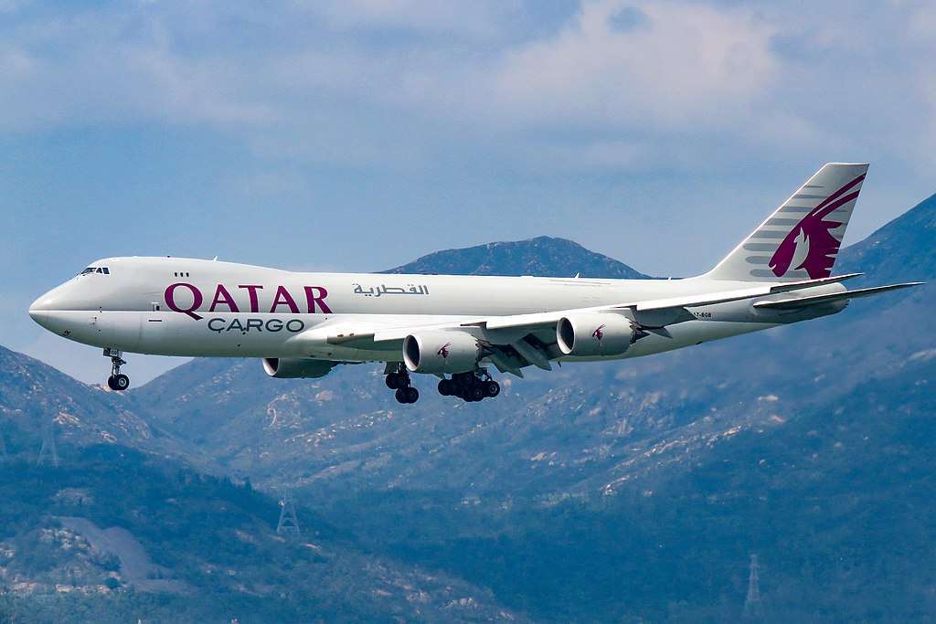 A Qatar Airways Cargo 747 freighter approaches over mountains.
