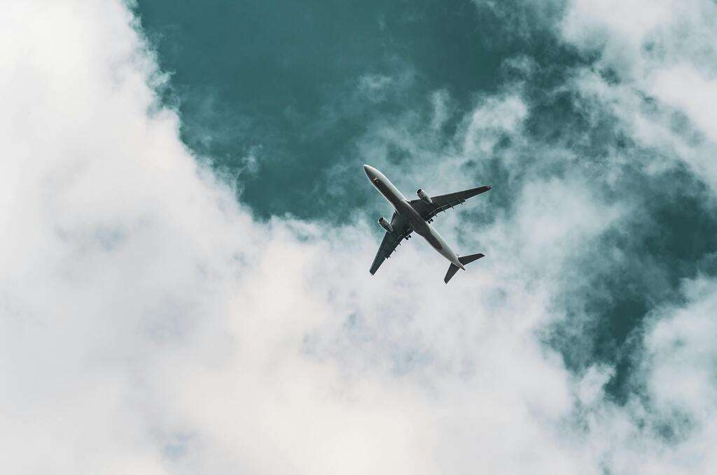 An airliner passes overhead in a cloudy sky.