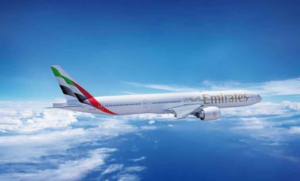 An Emirates Boeing 77 in flight above clouds.