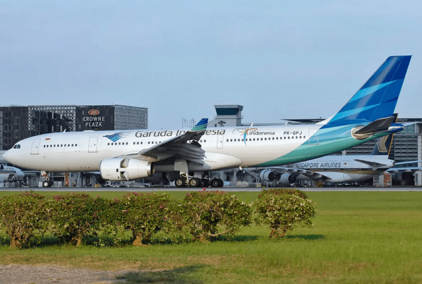 A Garuda Indonesia aircraft taxis past a parked Singapore Airlines jet.